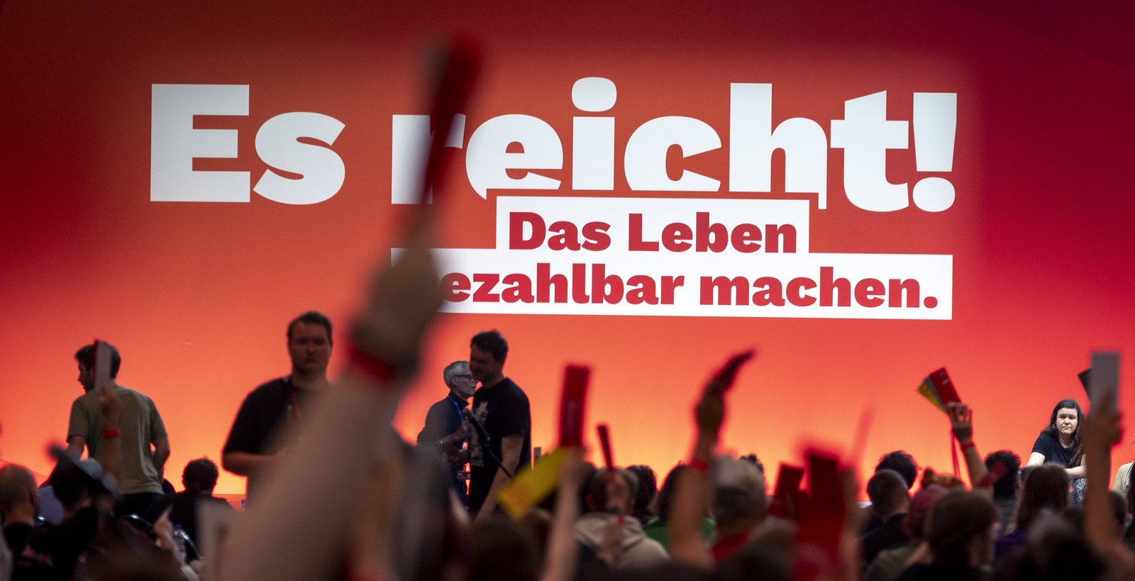 Der Slogan des Parteitags "Es reicht! Das Leben bezahlbar machen." auf einer roten Stellwand. Davor sieht man Hände, die Stimmkatrten in die Höhe halten.