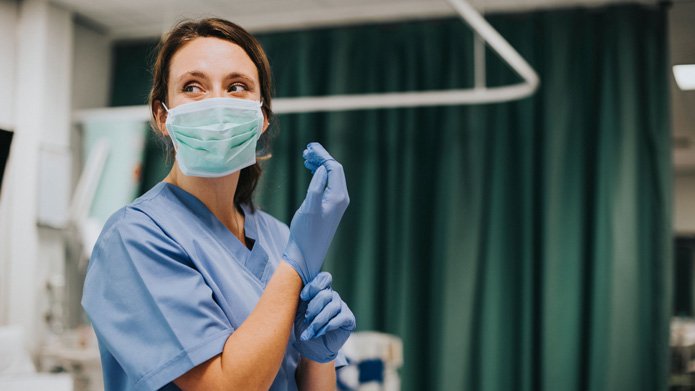 Female nurse with a mask putting on gloves