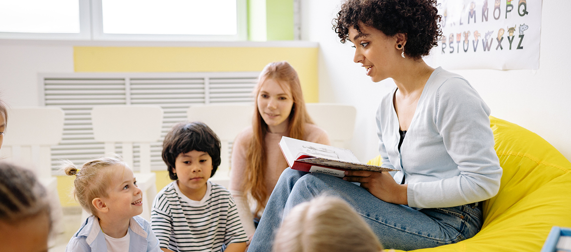Themenseiten_Header_Arbeit.jpg Erzieherin liest Kindern ein Buch vor
